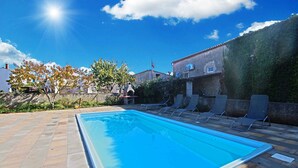 Et rektangulært swimmingpool med fliseterrasse, omgivet af liggestole.