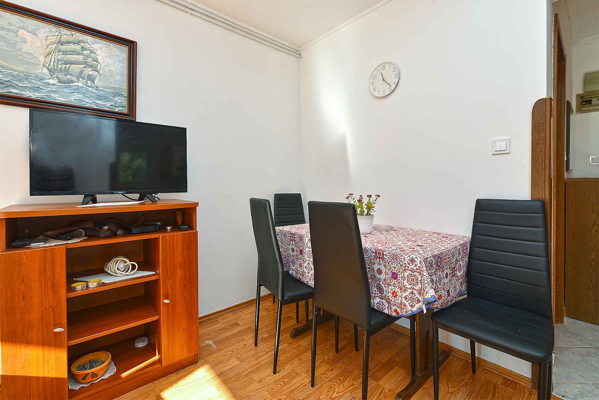 Een eetgedeelte met een houten kast, een televisie en een tafel met stoelen.