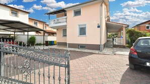 A two-story residential building with a balcony, a covered parking area, and a paved driveway. - Holiday apartment with air conditioning (Valbandon)
