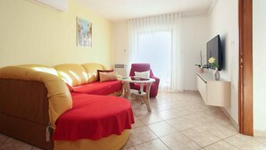 A living room with a sofa, a small table, a chair, a TV, and a window with curtains. - Holiday apartment with air conditioning (Banjole)