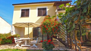 A two-story house with a patio area featuring a table and chairs, a potted plant with red flowers, and a staircase leading to the upper floor. - Holiday apartment with air conditioning (Banjole)