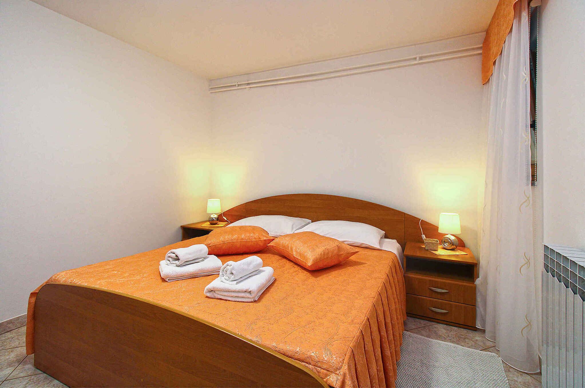 Un lit bien fait, avec une tête de lit marron, deux oreillers et deux serviettes pliées. On y trouve deux tables de chevet avec des lampes, et un radiateur est fixé au mur.