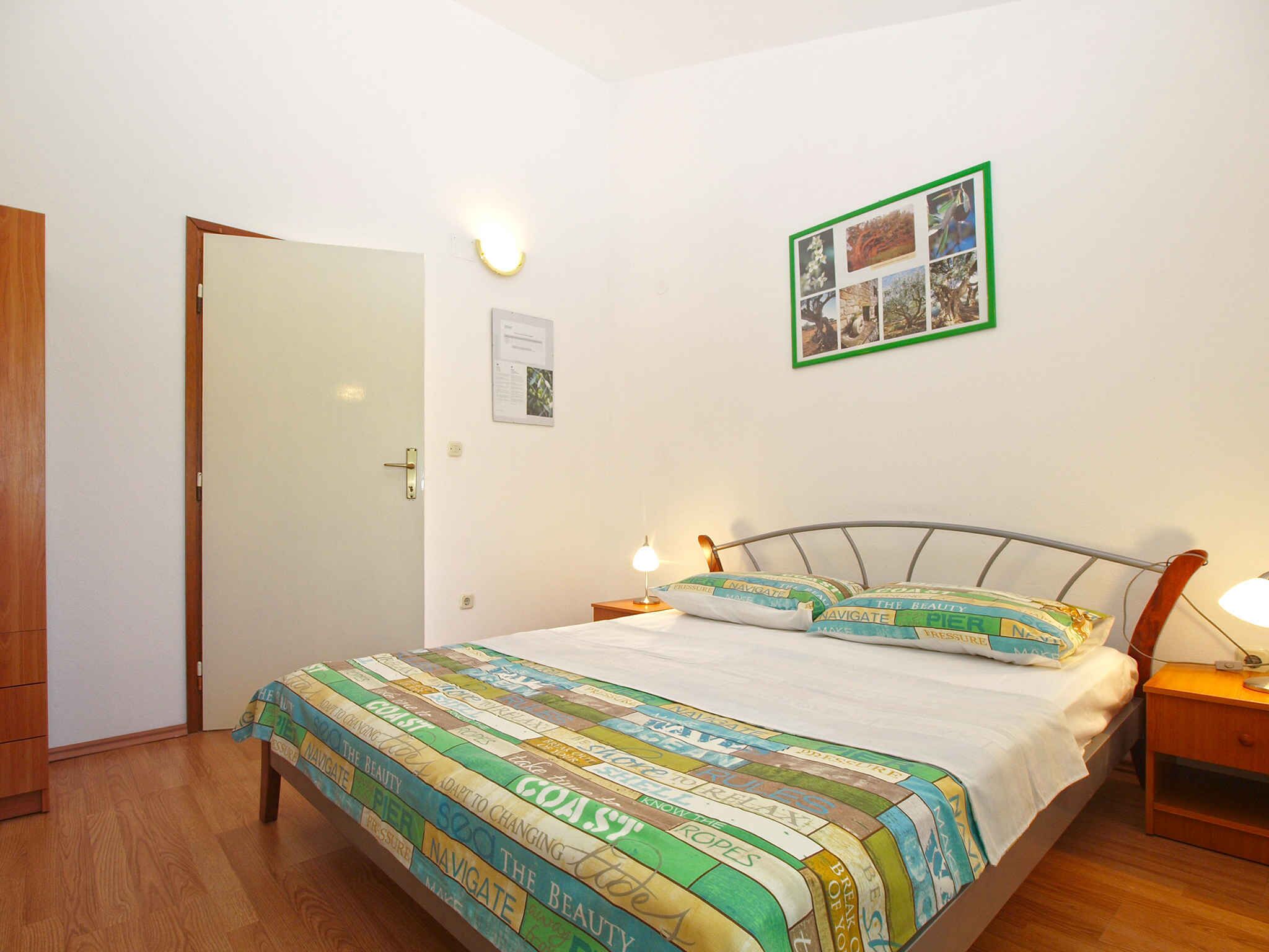 A bedroom with a bed, two bedside tables, a wall-mounted picture frame, and a door.