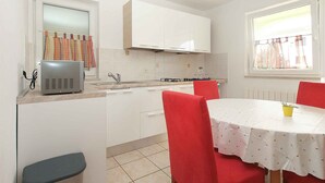 Una cocina compacta con armarios blancos, estufa a gas y comedor con mesa y sillas rojas.