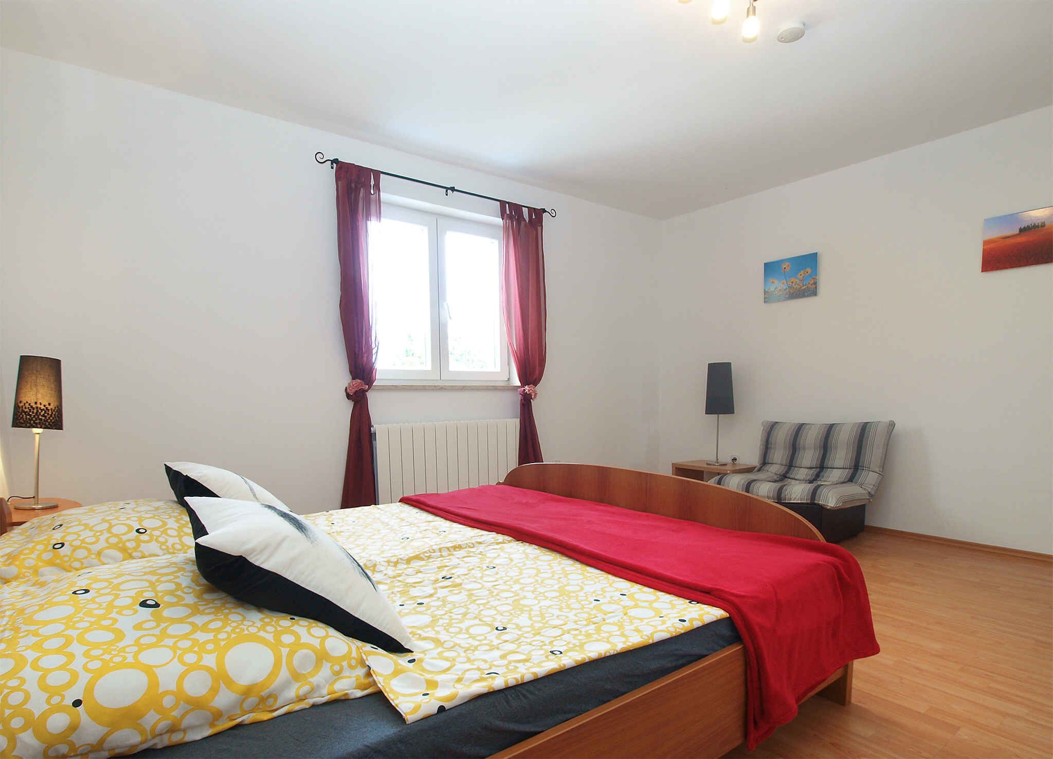 A bedroom with a bed, a chair, a window with curtains, a radiator, and a painting on the wall.