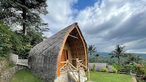 A thatched-roof hut with a wooden staircase leading to a door, surrounded by lush greenery and a stone wall. - Villa Bambu Rinjani & Restaurant By Zuzu (Bayan)