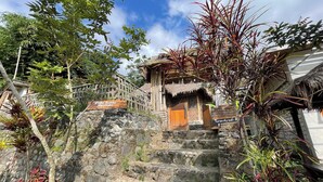 A stone staircase leading to a traditional wooden structure with a thatched roof, surrounded by lush greenery and a clear blue sky. - Villa Bambu Rinjani & Restaurant By Zuzu (Bayan)