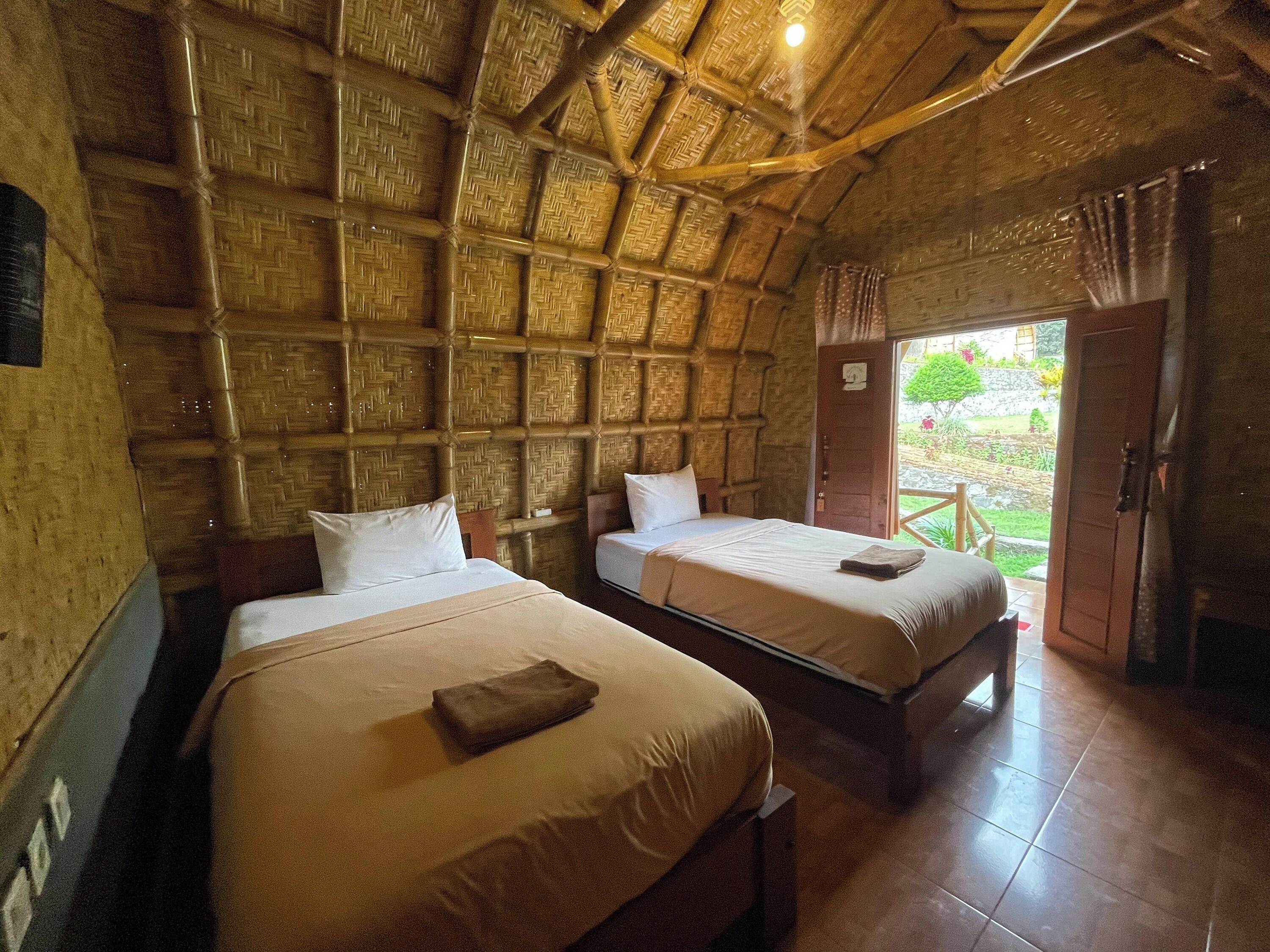 A room with two beds, a wooden ceiling, and a view of the garden.
