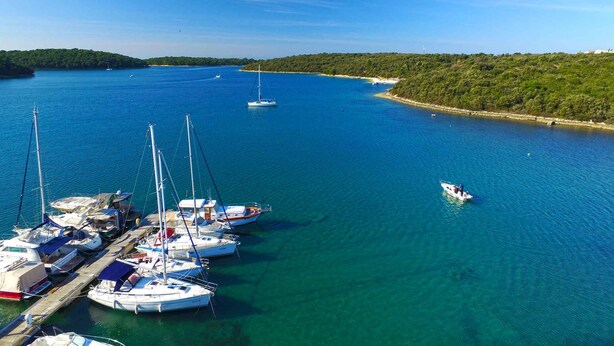 A marina with multiple sailboats docked, surrounded by clear blue water and a forested coastline. - Holiday apartment with terrace (Vinkuran)