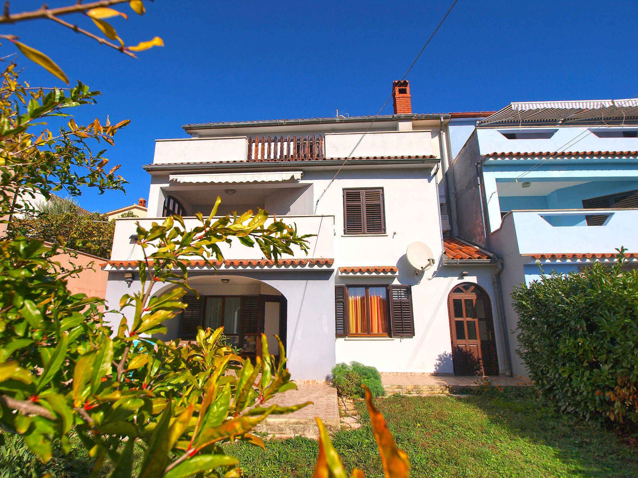 A two-story house with a white exterior, a tiled roof, and a small garden in front.