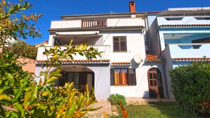 A two-story house with a white exterior, a tiled roof, and a small garden in front. - Holiday apartment with terrace (Vinkuran)