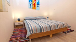 A bedroom with a wooden bed, striped bedding, a colorful woven rug, and a nightstand with a lamp. - Holiday apartment with terrace (Vinkuran)