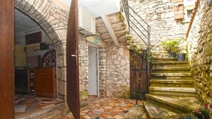 A courtyard with stone walls, a tiled floor, a wooden door, and a staircase leading to a balcony with potted plants. - Holiday home with air conditioning and terrace with barbecue (Medulin)