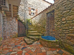 Ein Innenhof mit Steinmauern, einem Kachelboden, einem hölzernen Tor und einem kleinen, blau gefliesten Brunnen.