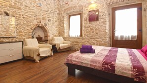 A bedroom with stone walls, a wooden floor, a bed with a floral bedspread, two chairs, a dresser, and a mirror. - Holiday home with air conditioning and terrace with barbecue (Medulin)