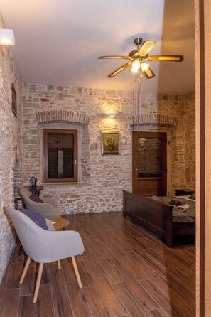 A room with stone walls, a wooden ceiling fan, a sofa, a chair, and a bed.