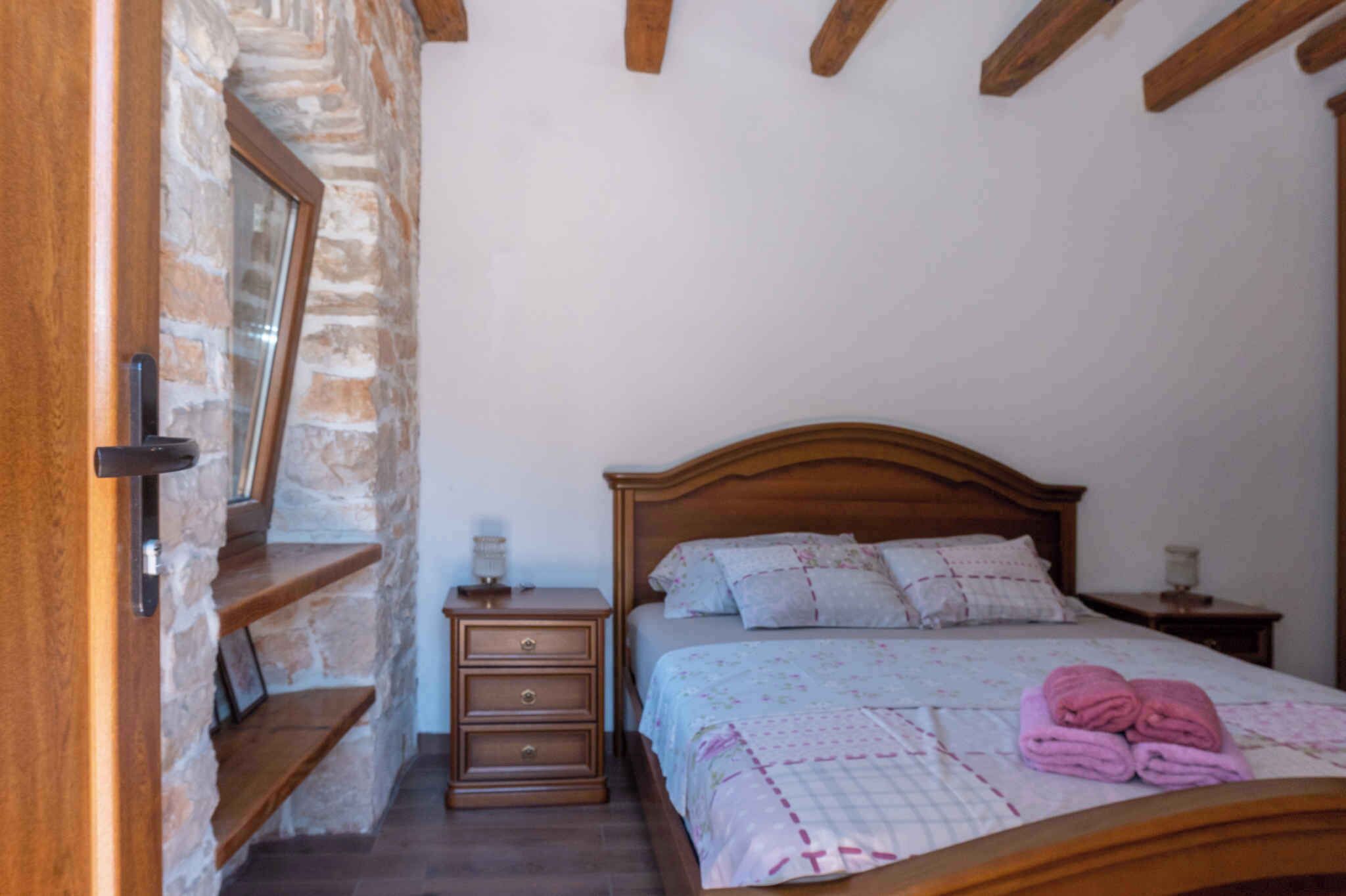 A bedroom with a wooden bed, a nightstand, a dresser, and a stone wall.