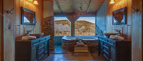 A bathroom with wooden walls, stone accents, two sinks, and a view of a mountainous landscape.