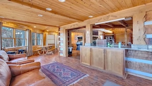 A spacious cabin interior with a wooden ceiling, a dining area with a bench and stools, a kitchen with a bar, and large windows. - Avoid The Traffic Jams 7acres 360 Views 7b 4 5b (Sevierville)