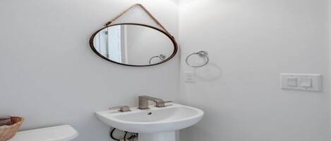 A bathroom with a white sink, a round mirror, and a toilet.