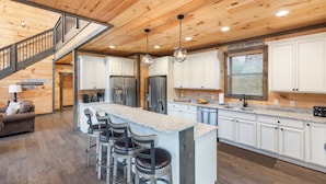A spacious kitchen with white cabinets, a central island with bar stools, stainless steel appliances, and a wooden ceiling. - Luxury Brand New Cabin 5b 5 5ba w Arcade Theater (Sevierville)