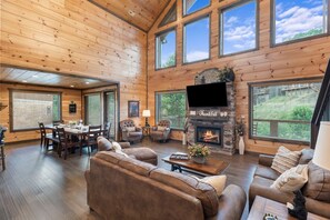 A spacious living room with a fireplace, wooden walls, and large windows. - Luxury Brand New Cabin 5b 5 5ba w Arcade Theater (Sevierville)