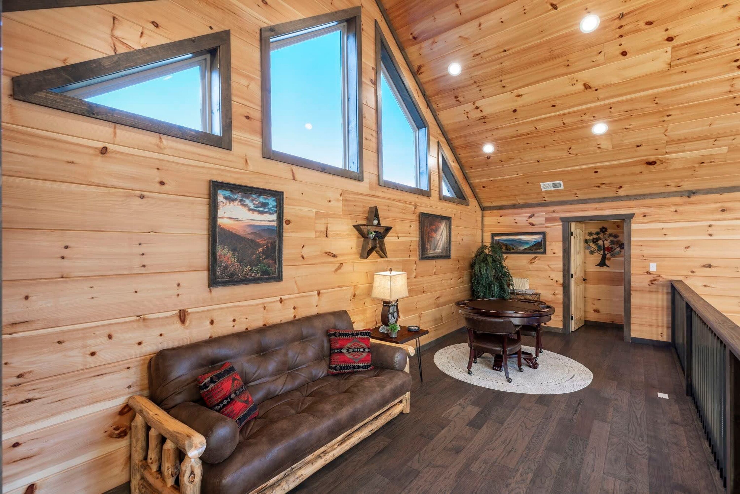 L’intérieur d’un chalet accueillant, avec un plafond en bois, de grandes fenêtres, un canapé en cuir, une table à manger et une cheminée.