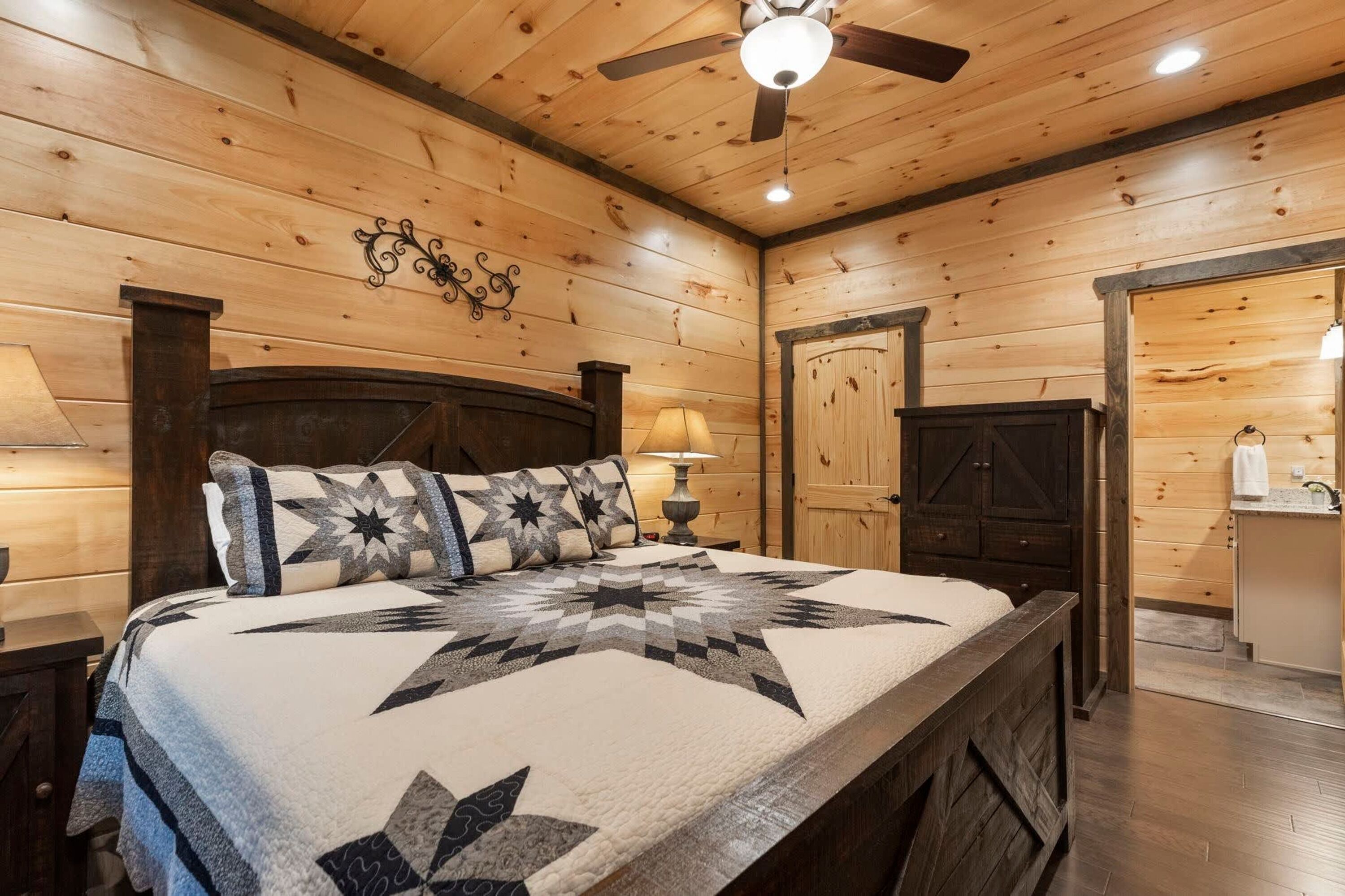 Dormitorio con paneles de madera, una cama, ventilador de techo y mesita de noche.