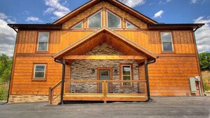 A two-story wooden house with a stone facade, a central entrance with a staircase, and a fenced front yard. - Luxury Brand New Cabin 5b 5 5ba w Arcade Theater (Sevierville)