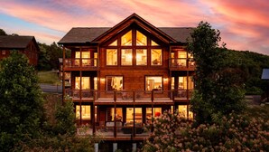 A large, multi-story wooden house with a balcony on the second floor, surrounded by lush greenery. - Luxury Brand New Cabin 5b 5 5ba w Arcade Theater (Sevierville)