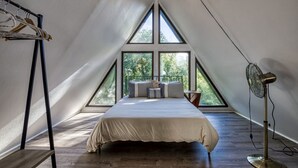 A bedroom with a large bed, a standing fan, and a window overlooking greenery. - Unique 4bed 3bath A-frame (Kodak)