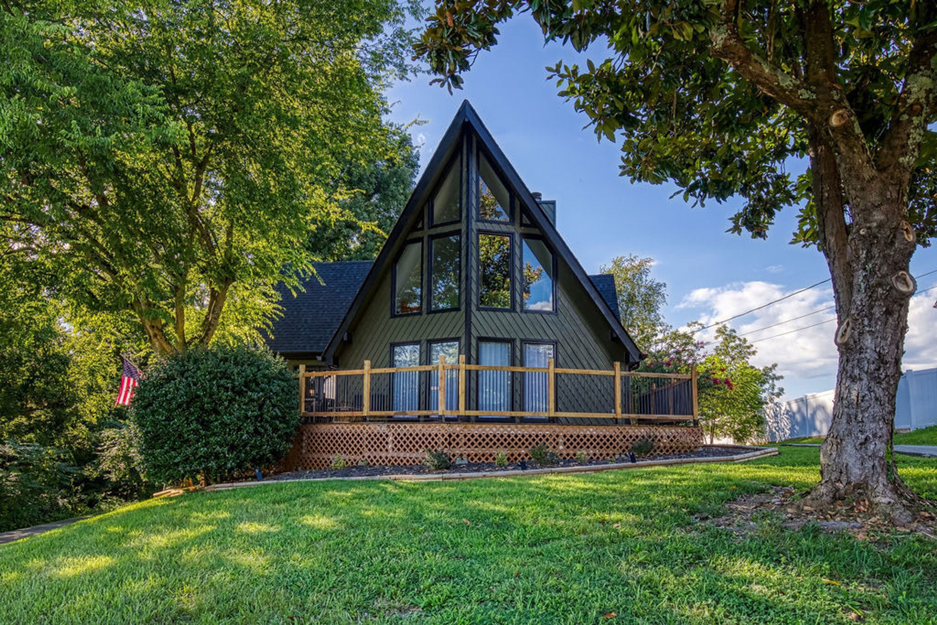 A house with a triangular roof, a wooden deck, and a well-maintained lawn.