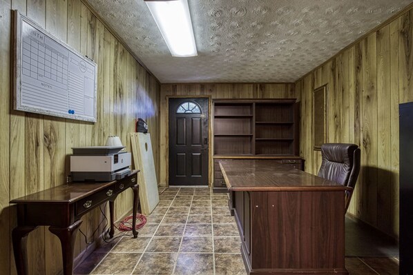 Quarto com paredes de madeira, uma escrivaninha, uma cadeira, uma porta e um mural.