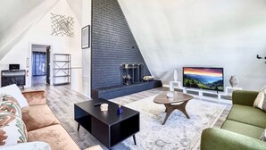 A modern loft apartment with a high ceiling, a fireplace, a television, and a cozy seating area. - Unique 4bed 3bath A-frame (Kodak)