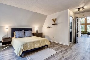 Un dormitorio con cama, mesitas de noche, una repisa en la pared y una puerta que da a otra habitación.
