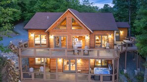 A two-story wooden cabin with a balcony, a hot tub, and a stone wall. - Luxury 3 2 5 Cabin Lake Views Theatre Gameroom (Bryson City)