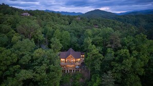 A large, two-story house surrounded by dense forest, with a prominent balcony and multiple windows. - Luxury 3 2 5 Cabin Lake Views Theatre Gameroom (Bryson City)