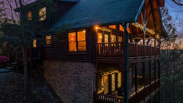 Eine Holzhütte mit Balkon und Lichterkette, umgeben von Bäumen.