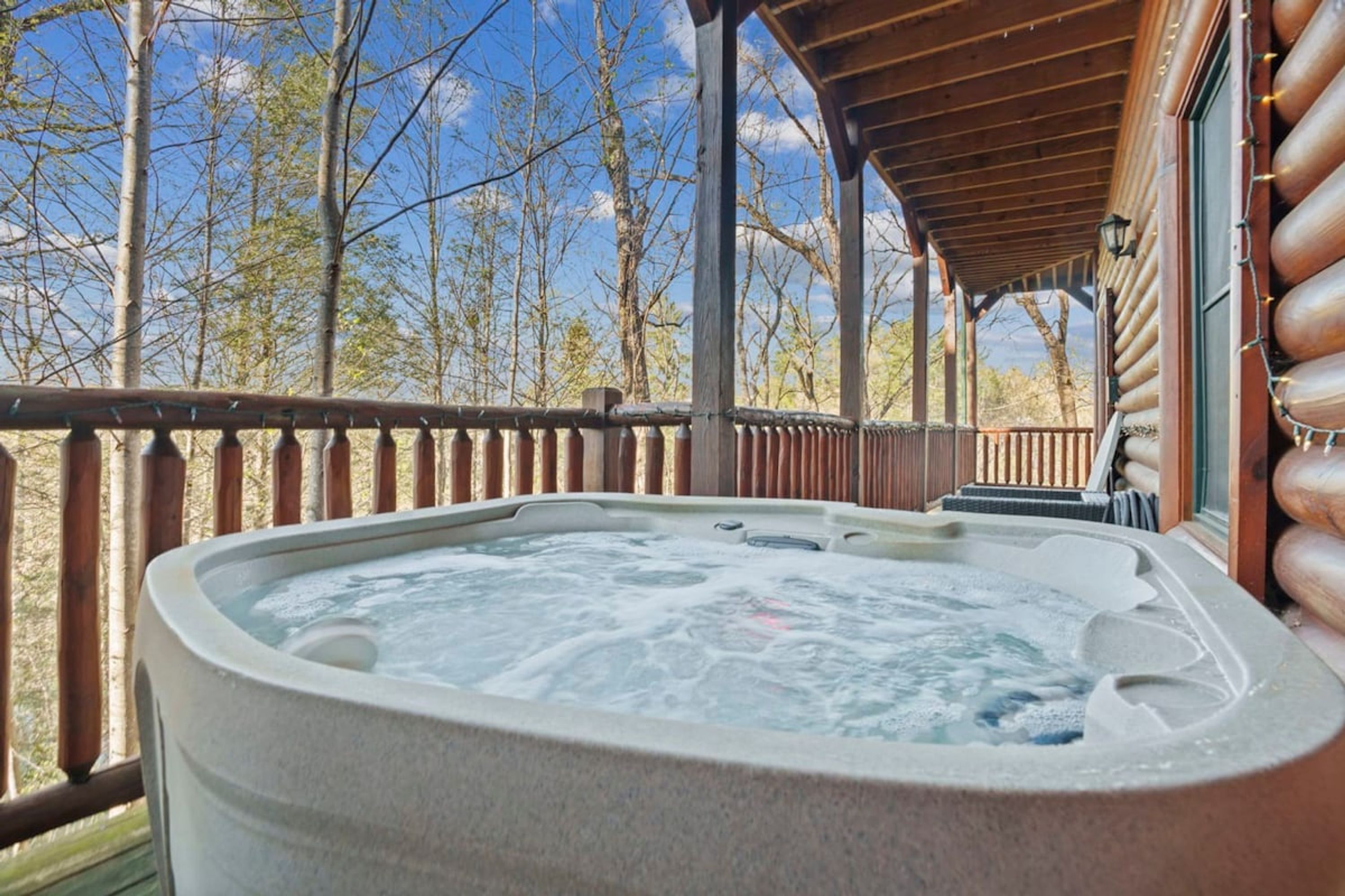 A hot tub on a wooden deck with a view of trees and a clear sky.