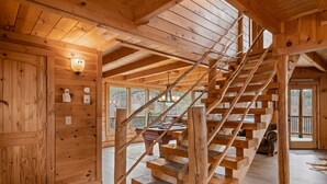 A wooden staircase with a handrail, a wall-mounted light fixture, and a pool table in the background. - 47majestic Luxe 3bd 3 5ba w Spectacular Views (Sevierville)