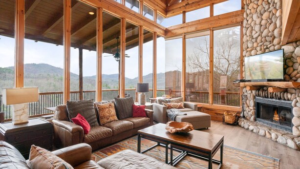 A spacious living room with a stone fireplace, leather sofas, and large windows offering a mountain view. - 47majestic Luxe 3bd 3 5ba w Spectacular Views (Sevierville)
