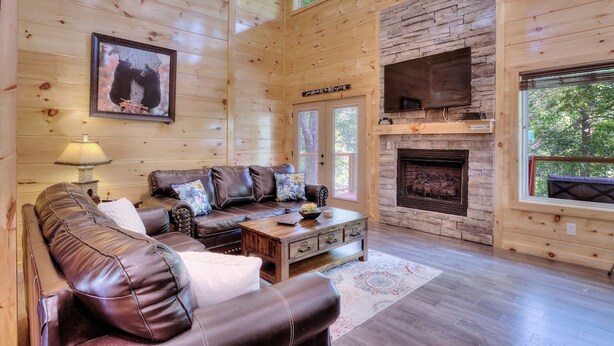 A cozy cabin interior with a leather sofa, a fireplace, and wooden walls. - 5 Master Suites 5 6bath Cabin 5 min to Gsmnp (Gatlinburg)