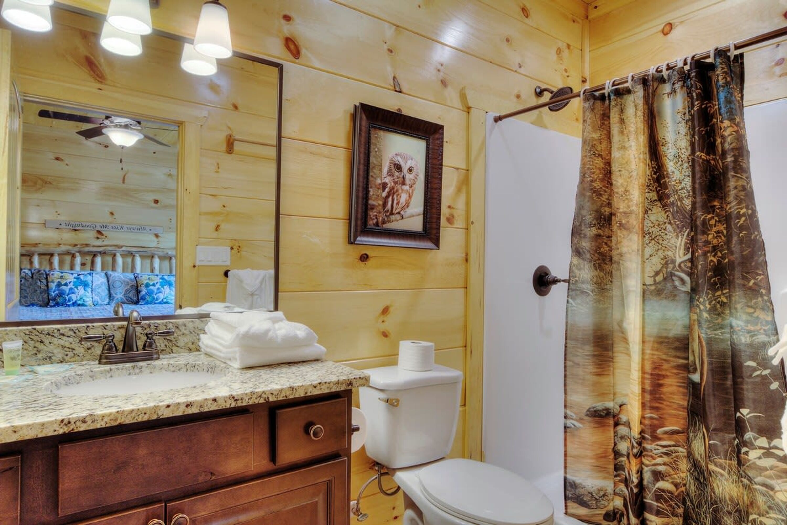 A bathroom with wooden walls, a framed owl picture, a sink with a marble countertop, and a shower curtain with a nature design.