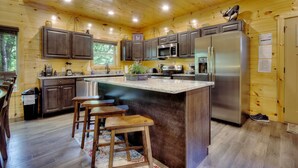 A modern kitchen with wooden cabinetry, stainless steel appliances, and a central island with bar stools. - 5 Master Suites 5 6bath Cabin 5 min to Gsmnp (Gatlinburg)