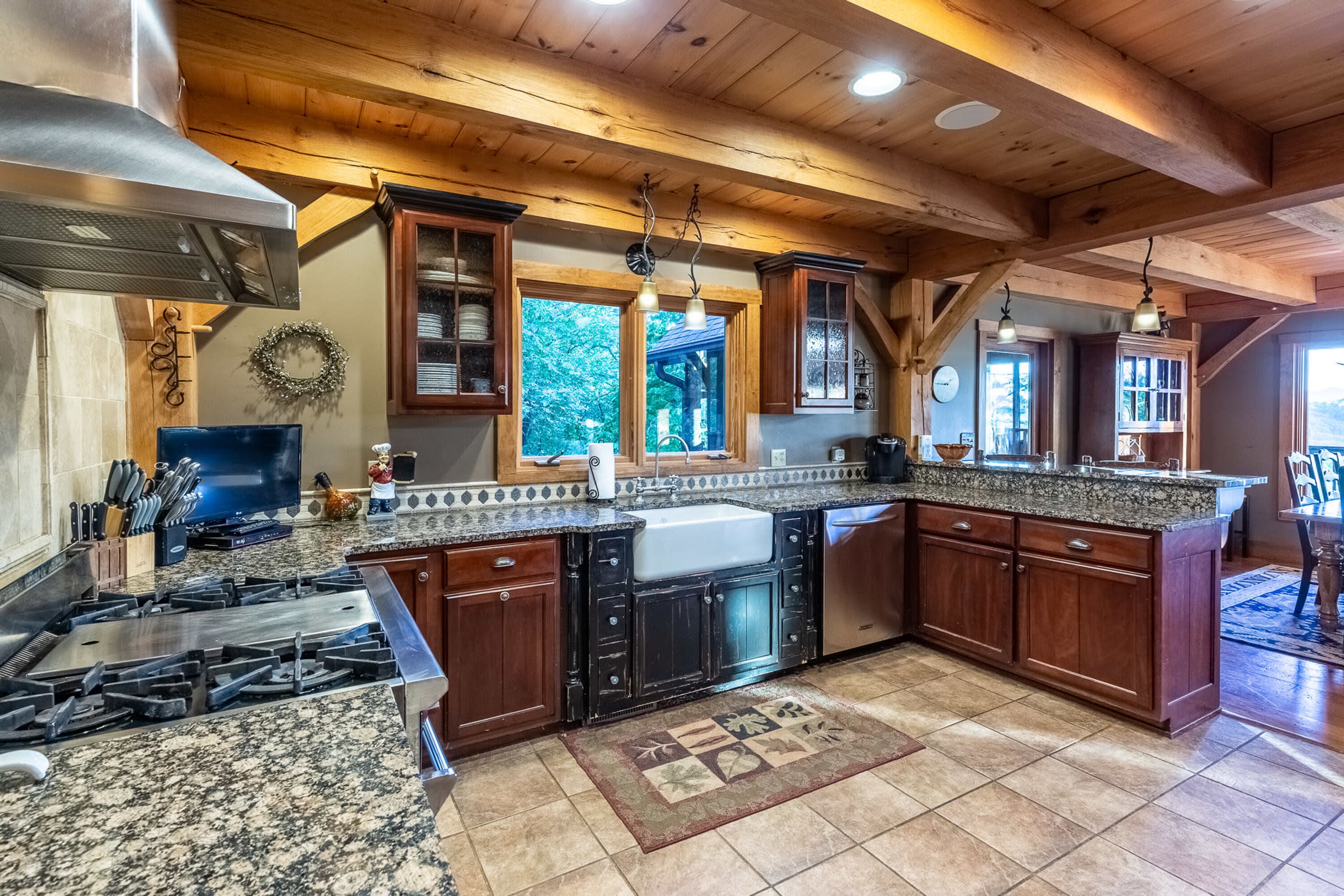 A kitchen with granite countertops, wooden cabinets, a stainless steel range hood, and a large island with a sink.