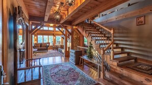 A spacious interior with a wooden staircase, a cozy seating area, and a large window offering a view of the outdoors. - Lake Views Luxury Hottub Game Rm 5bed 4 5bath (Bryson City)