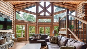 Ein Blockhaushaus-Interieur mit Kamin aus Stein, einem Ledersofa und einem an der Wand montierten Fernseher.