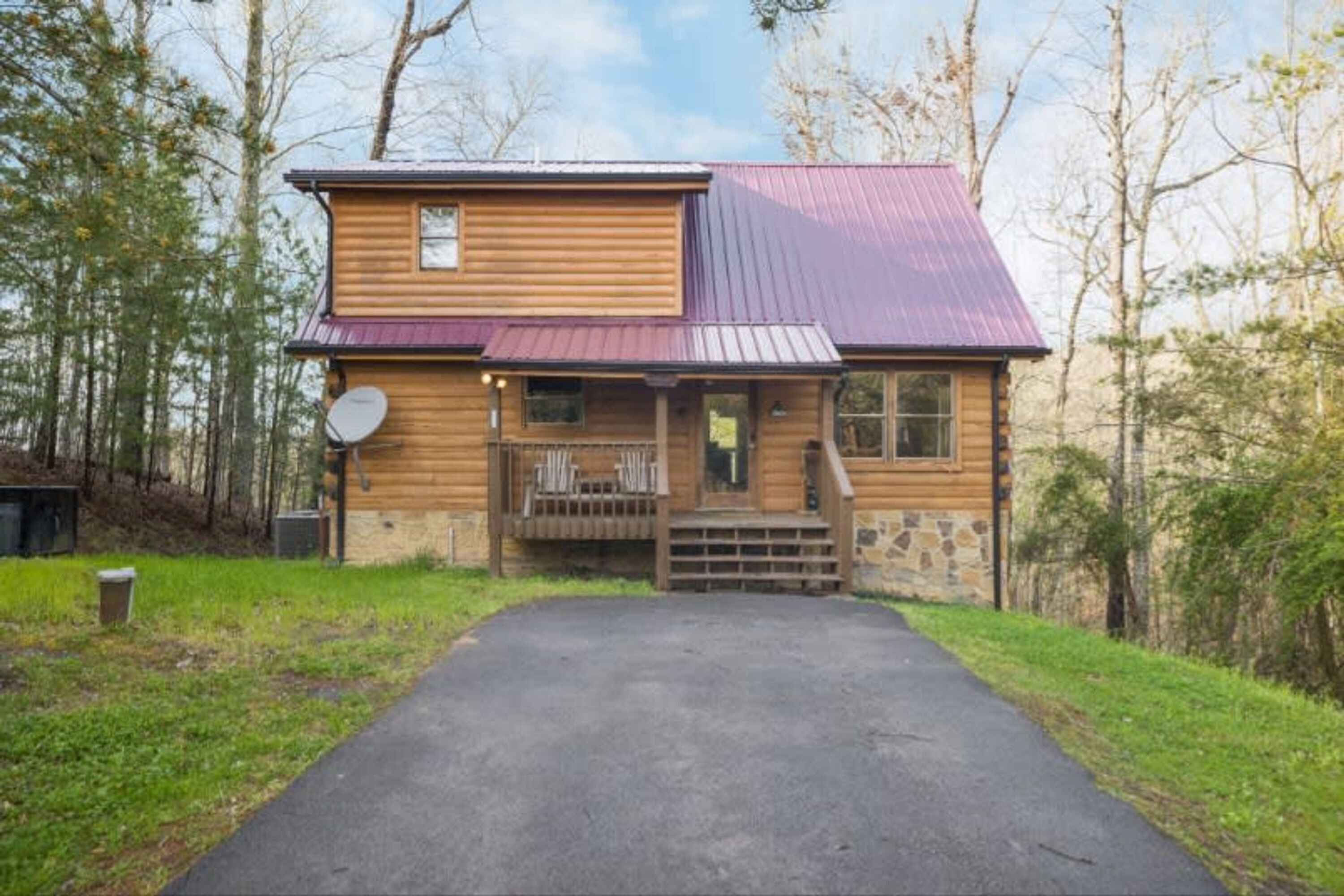 A two-story log cabin with a metal roof, a front porch with chairs, and a satellite dish.