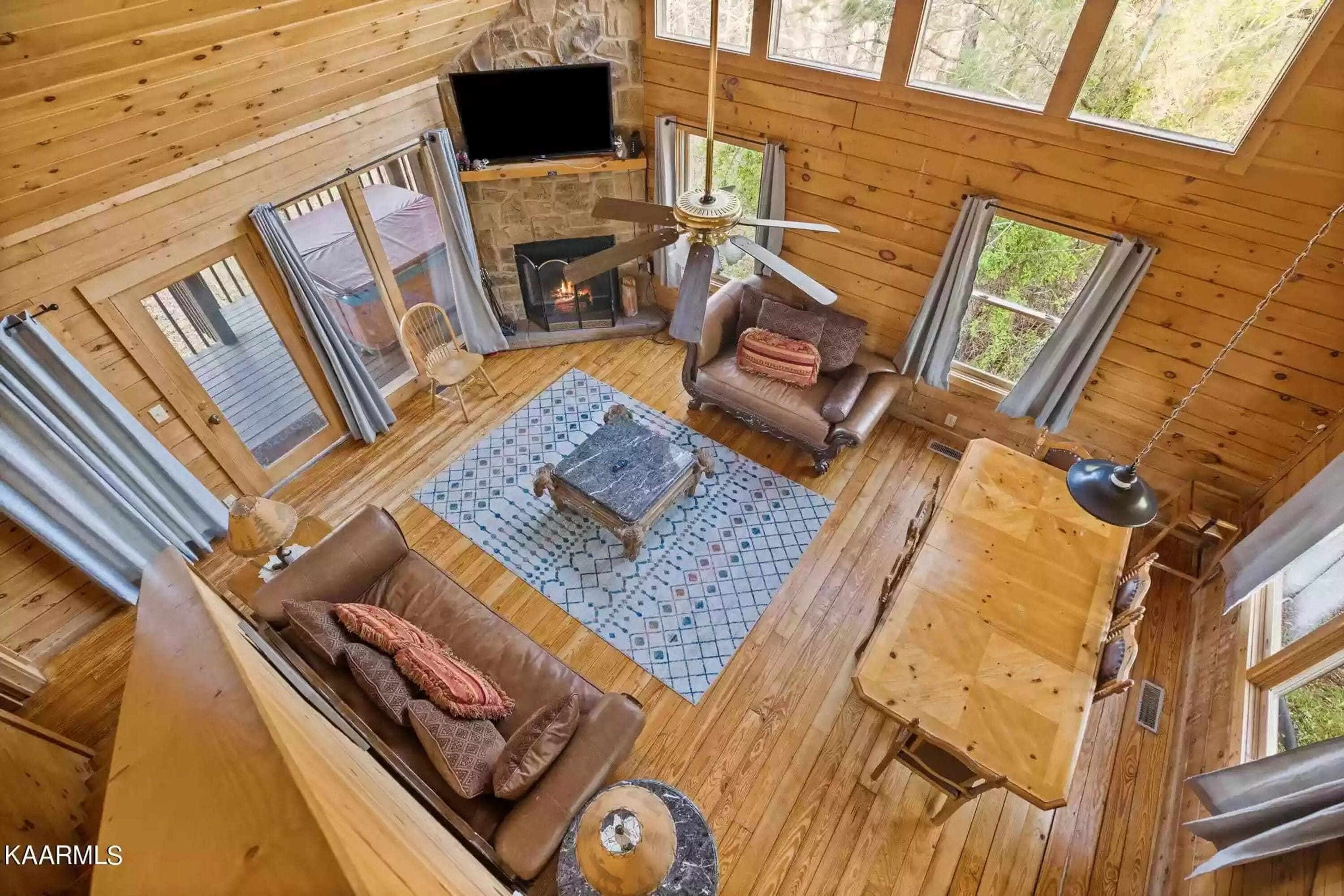 A cozy cabin interior with a stone fireplace, wooden furniture, and large windows.