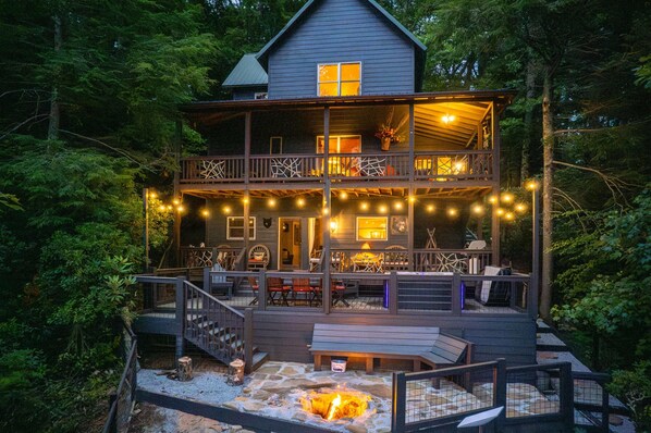 A two-story wooden cabin with a deck, outdoor seating, and a fire pit.